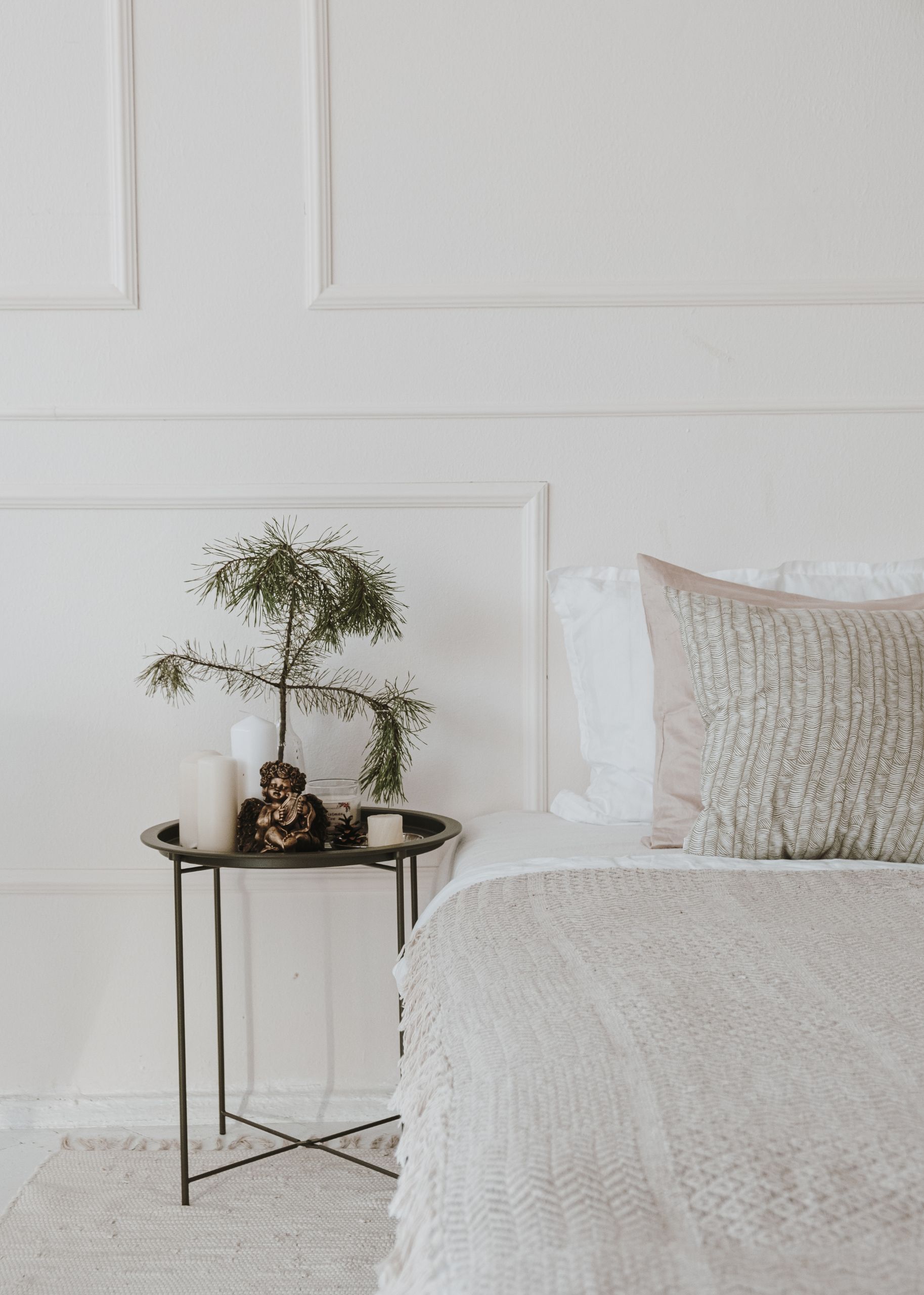 Mesita auxiliar metálica con bandeja, plantas y decoración junto a cama blanca