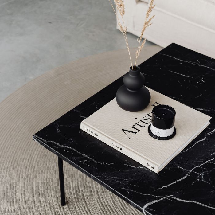 Mesa de mármol negro con libro de arte, café y florero minimalista