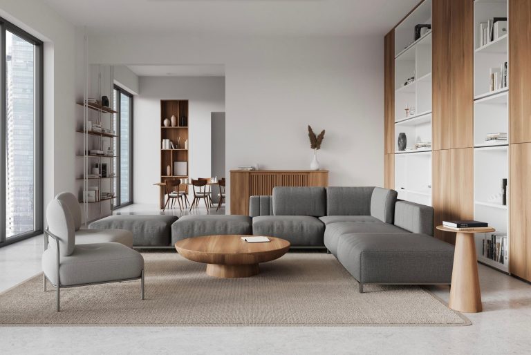 Salón moderno con sofá gris modular, mesa redonda de madera, estanterías y elementos decorativos