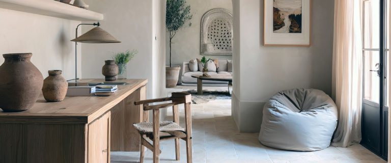 Espacio de trabajo moderno con escritorio de madera, silla, puf gris y decoración natural